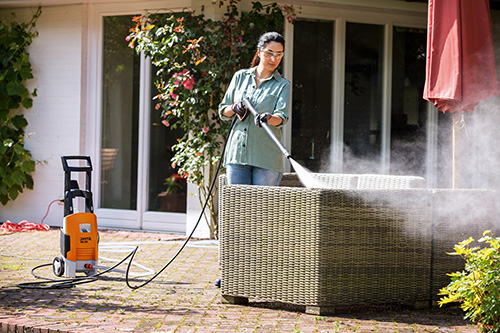 Mujer limpiando los muebles de la terraza con máquina de agua a presión